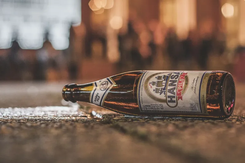 Stimmungsvolle Produktfotografie einer Hansa Pils Bierflasche in warmer Atmosphäre. Professionelle Aufnahme aus der Bodenperspektive mit künstlerischem Bokeh-Effekt. Authentische deutsche Bierkultur in 1536x1024 Pixel Auflösung.
