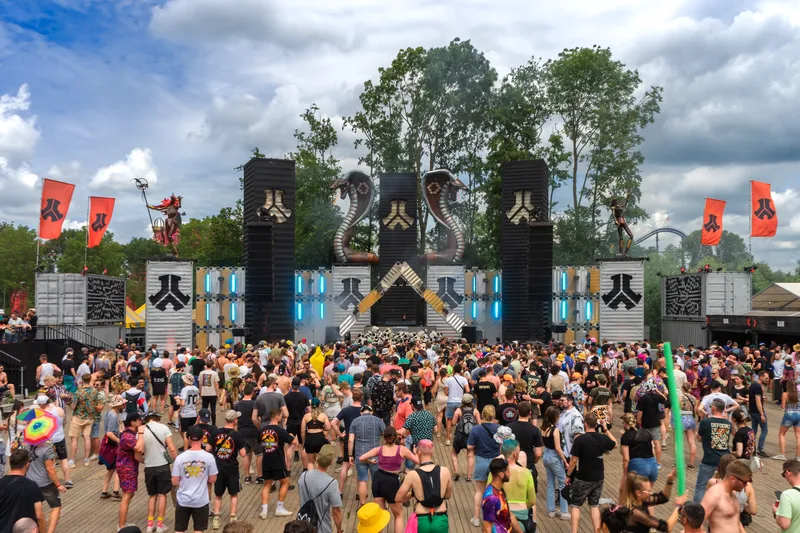 Atmosphärische Festivalaufnahme einer imposanten EDM-Bühne mit charakteristischen Cobra-Skulpturen, LED-Installationen und roten Bannern vor begeisterter Festivalmenge. Professionelle Eventfotografie in hoher Auflösung (1536x1024) zeigt die energiegeladene Atmosphäre eines modernen Musikfestivals.
