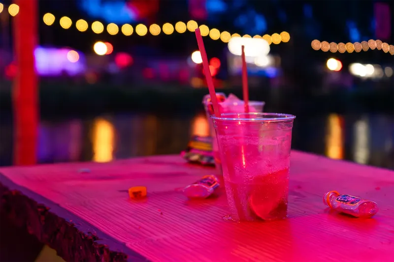 Atmosphärisches Nachtleben-Foto: Erfrischendes pinkes Cocktailgetränk auf beleuchteter Bar-Oberfläche, umrahmt von stimmungsvollen Lichterketten und Club-Ambiente. Perfekte Visualisierung für Nightlife, Party und Unterhaltung.
