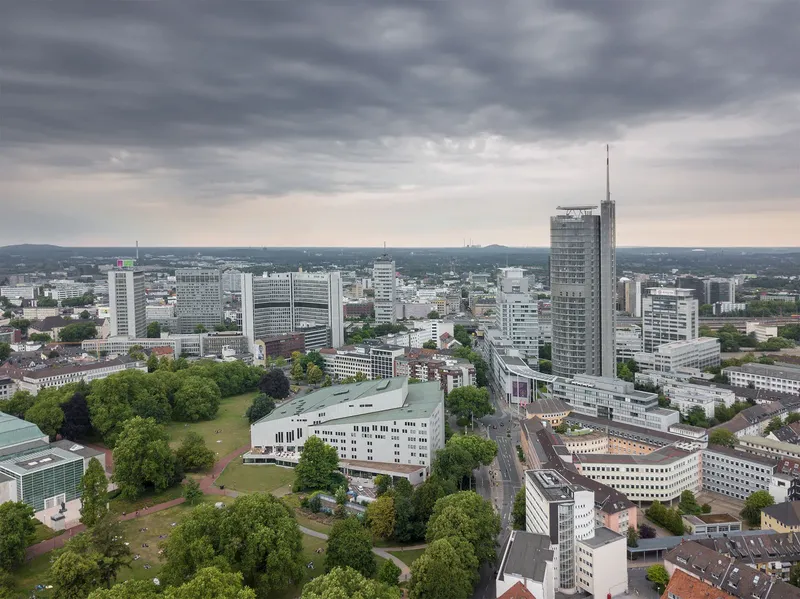 Spektakuläre Luftaufnahme der Essener Skyline mit dem ikonischen RWE-Tower, der modernen Philharmonie und dem urbanen Stadtbild unter dramatischem Wolkenhimmel. Zeigt die perfekte Symbiose aus Kultur, Wirtschaft und Architektur im Herzen des Ruhrgebiets.
