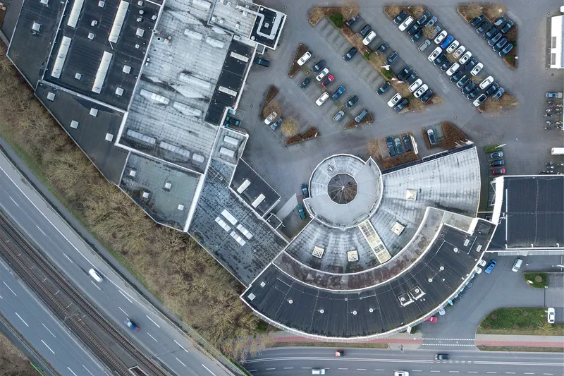 Modernes Autohaus mit einzigartiger Rundarchitektur aus der Vogelperspektive. Großzügiger Parkplatz, erstklassige Verkehrsanbindung und professionelle Fahrzeugpräsentation in zeitgemäßem Ambiente. Standort direkt an Hauptverkehrsstraße mit Schienen- und Straßenanbindung.
