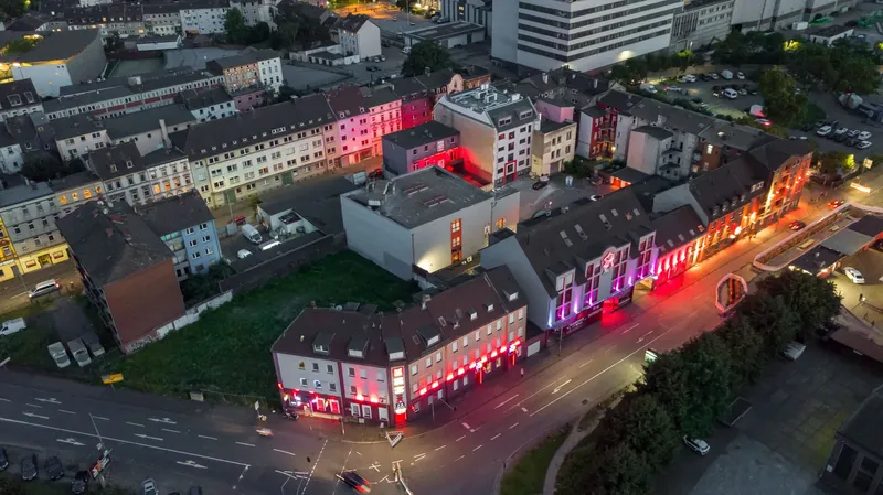 Atmosphärische Luftaufnahme des Duisburger Rotlichtviertels bei Nacht. Eindrucksvolle urbane Nachtfotografie mit charakteristischer roter Neonbeleuchtung, historischen Gebäuden und städtischer Infrastruktur im Ruhrgebiet. Authentischer Einblick in das nächtliche Stadtleben Duisburgs.
