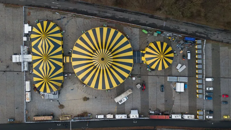 Spektakuläre Drohnenaufnahme der ikonischen schwarz-gelb gestreiften Zirkuszelte von Flic Flac: Ein faszinierender Blick von oben auf das moderne Zirkusensemble mit seinem charakteristischen Design und der einzigartigen geometrischen Anordnung der drei Zelte am Wasser.