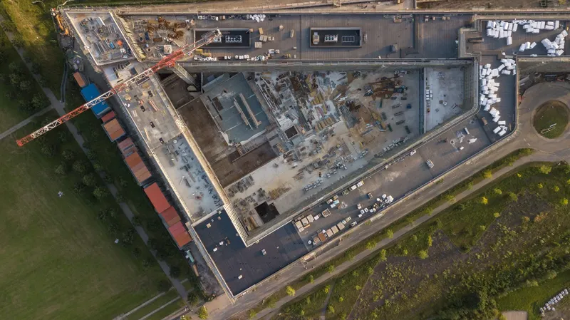 Exklusive Luftaufnahme des Materna Hauptsitzes in der Bauphase: Moderner Architekturkomplex mit laufenden Bauarbeiten, umgeben von Grünflächen. Drohnenaufnahme zeigt eindrucksvoll die Dimension des Bauprojekts mit Baukran und fortschreitenden Konstruktionsarbeiten.
