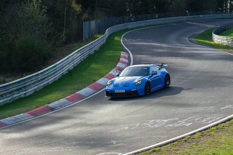 Erleben Sie die Dynamik des Nürburgrings mit einem blauen Porsche, der eine Kurve auf der legendären Rennstrecke in Deutschland meistert. Perfekt für Motorsport-Enthusiasten und Liebhaber von Sportwagen.
